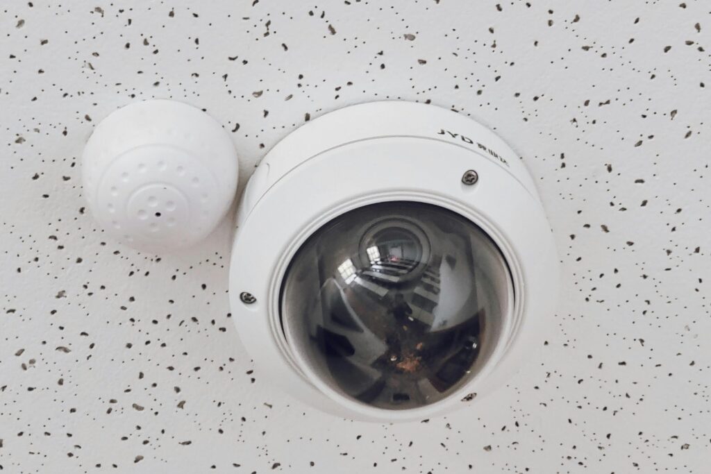 Close-up of a round dome surveillance camera installed on a speckled ceiling for security monitoring.